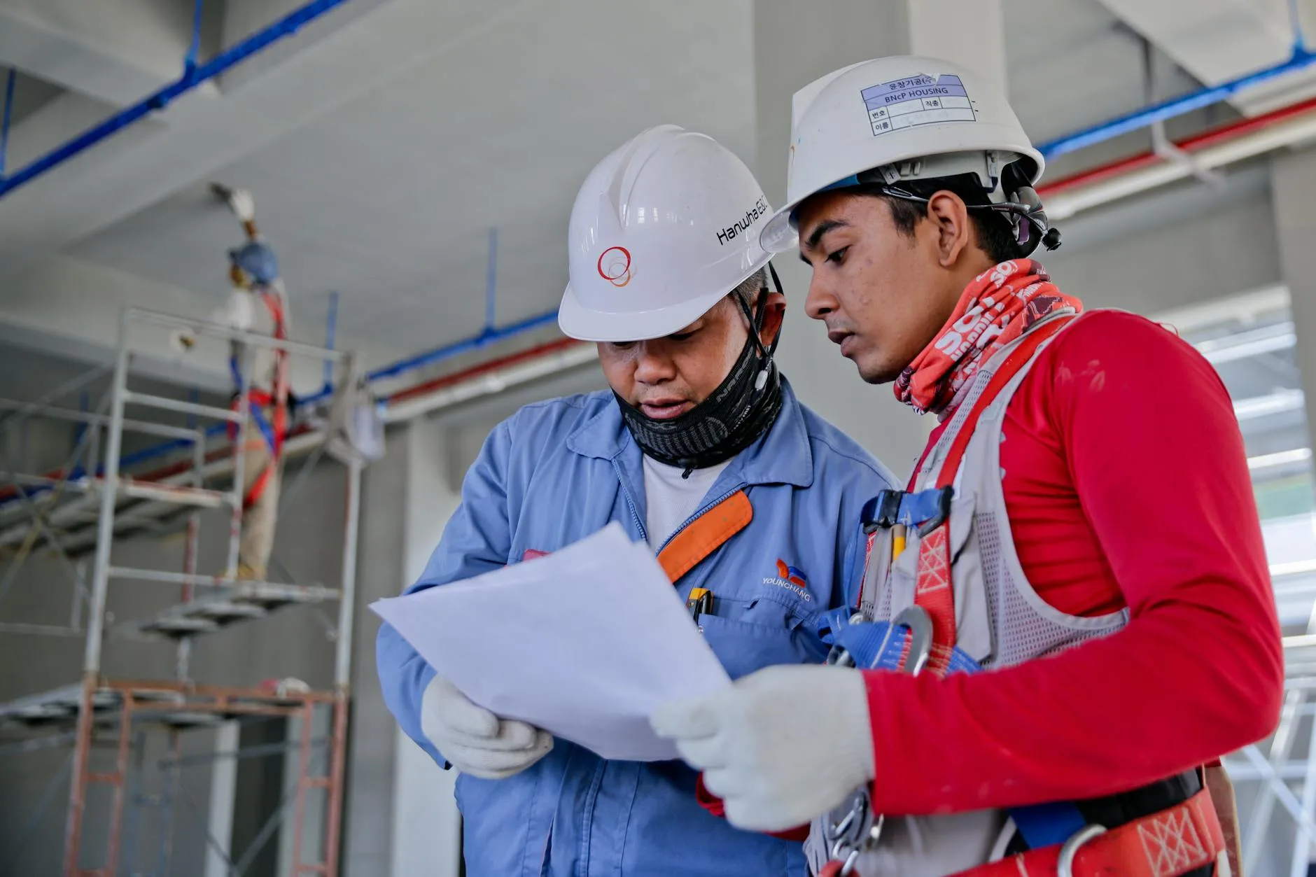 Induksi keselamatan untuk personel yang bekerja di kapal 2 Two engineers in safety helmets reviewing construction plans at a worksite.