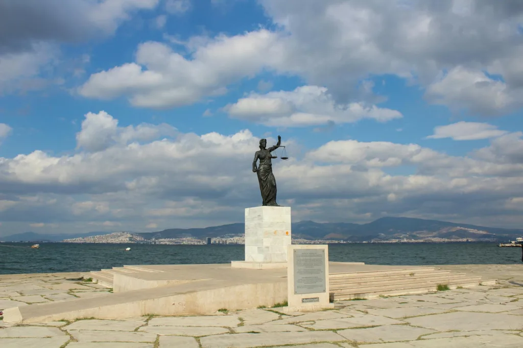 Apa Itu Empat Pilar Aturan Laut? 4 Lady Justice statue situated by a scenic coastal landscape under a vibrant blue sky.