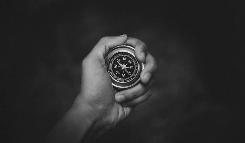 A black and white close-up of a hand holding a compass, symbolizing exploration.